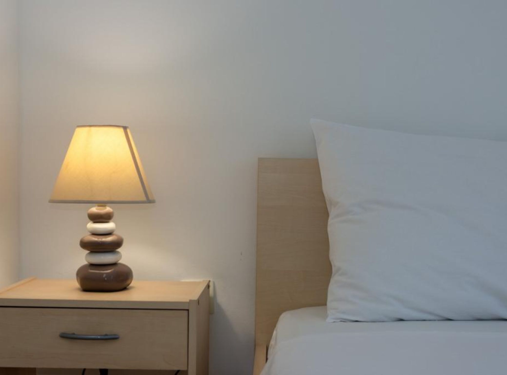 A bed with a white pillow and a bedside table with a lamp.