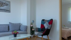 Ein modernes Wohnzimmer mit grauem Sofa, einem Glastisch, einem farbenfrohen Sessel und einer Topfpflanze.