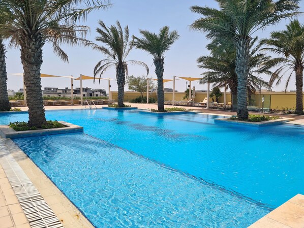 Une piscine à l’eau d’un bleu cristallin, entourée de palmiers et de chaises longues.