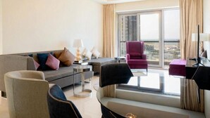 A modern hotel room with a sofa, armchairs, a coffee table, and a view of the city through large windows. - Beachfront Apartment (Lusail)