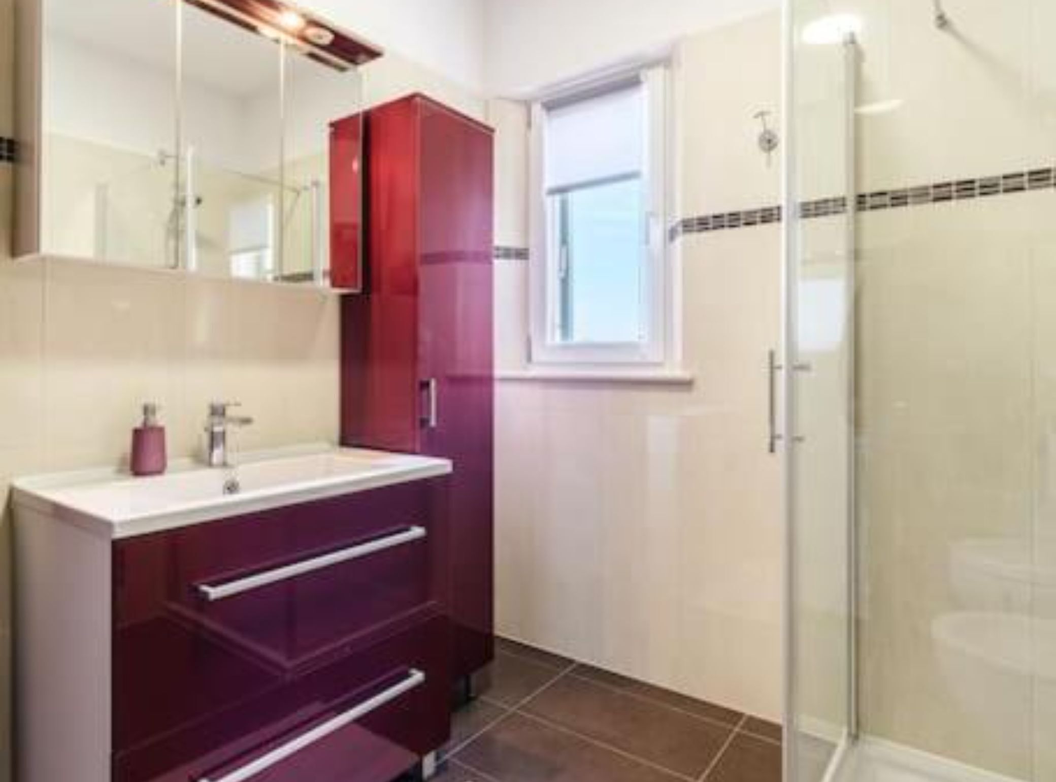 A modern bathroom with a glass shower enclosure, a vanity with a mirror, and a window providing natural light.