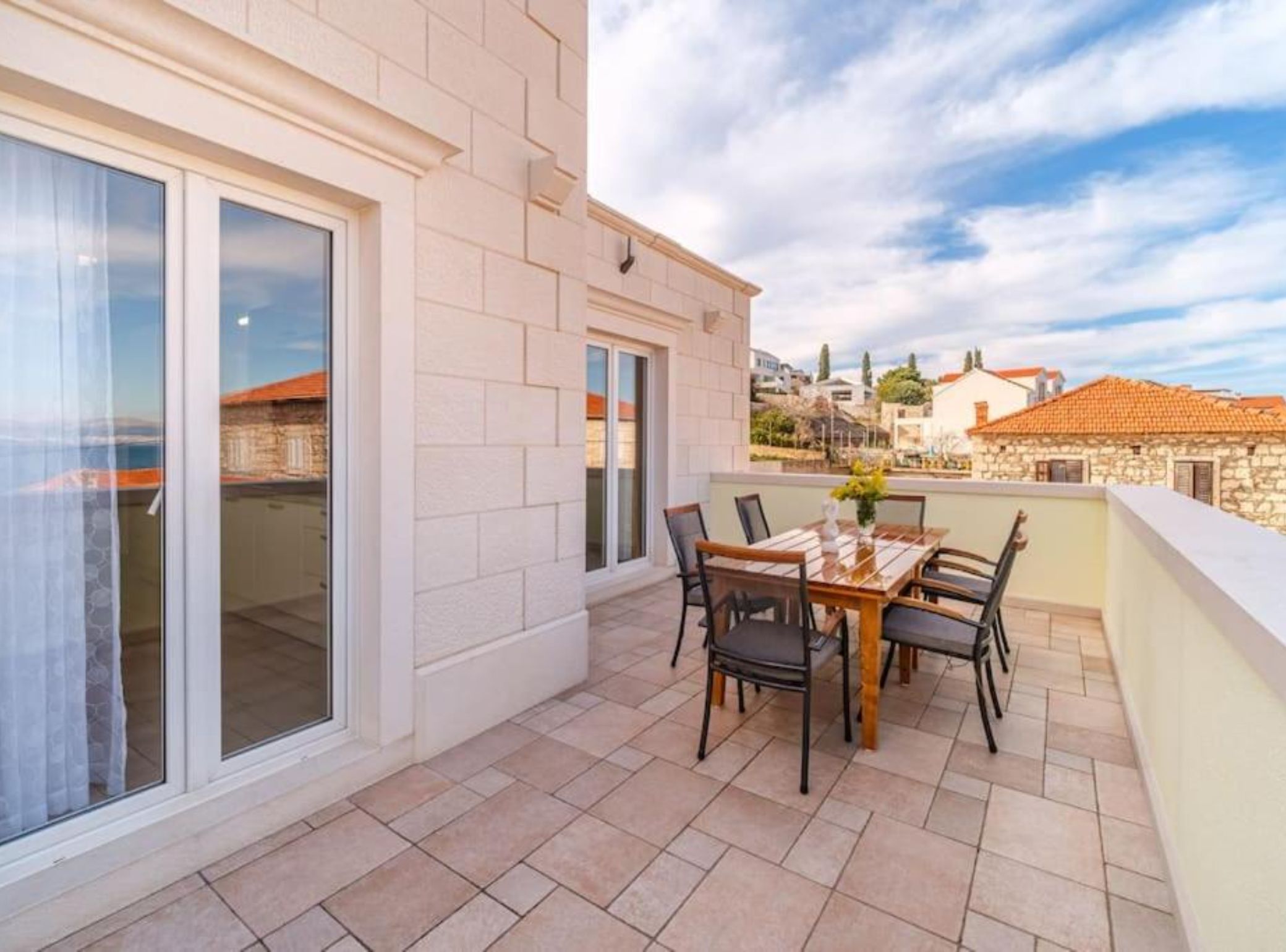 A balcony with a table and chairs, a view of the city, and a stone building in the background.