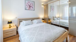 A bedroom with a large bed, bedside tables, a mirror, and a floral painting on the wall. - Sutivan Sea Terrace Apartment (Sutivan)