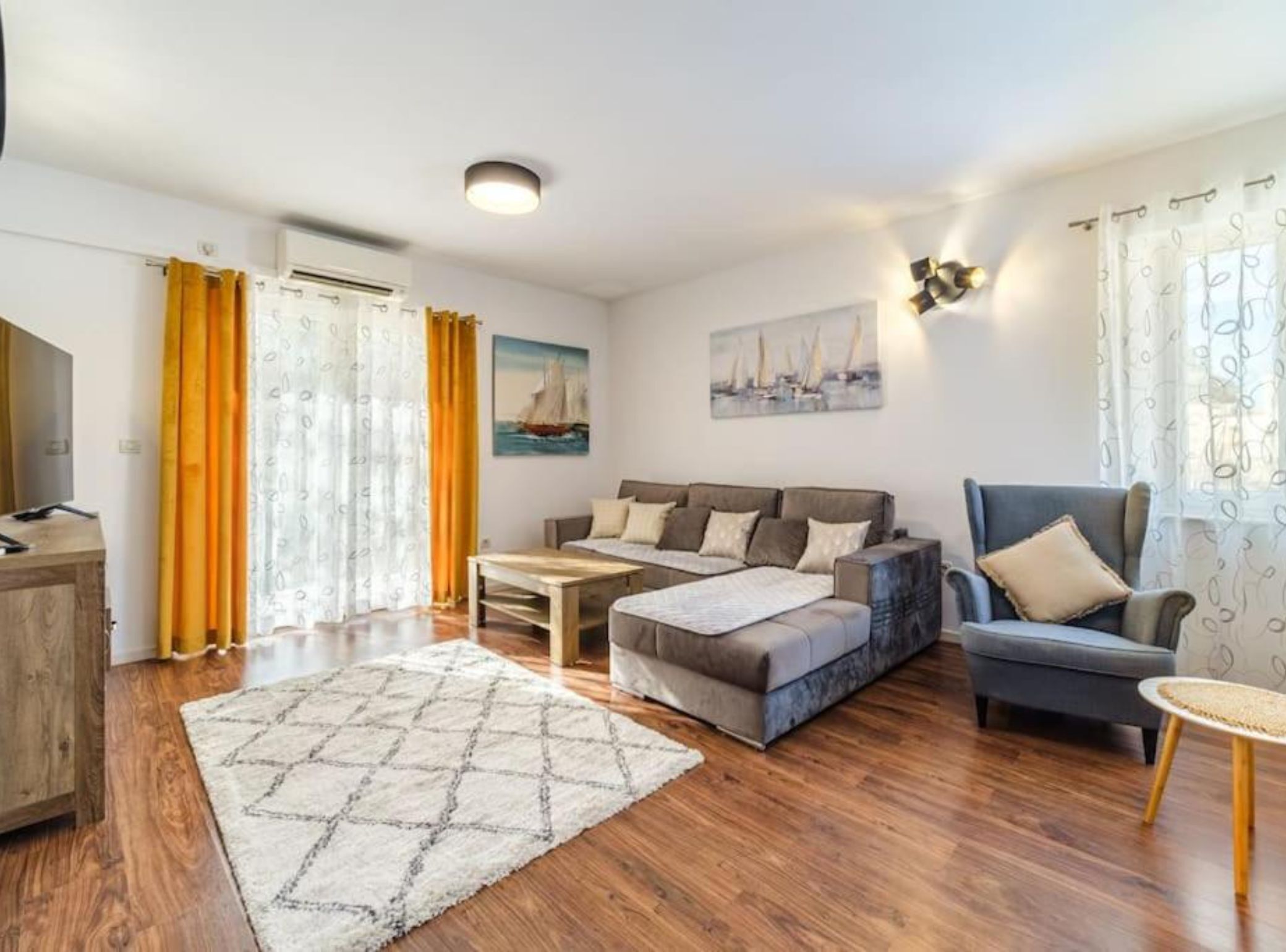 A modern living room with a sofa, a coffee table, and a chair. There is a wooden cabinet and a rug on the floor.