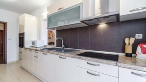 A modern kitchen with white cabinets, a stainless steel range hood, a double sink, and a microwave. - Sutivan Sea Terrace Apartment (Sutivan)
