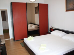 Een hotelkamer met een bed, een nachtkastje, een rode garderobe en een schilderij aan de muur.