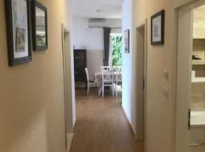 Een gang met ingelijste foto’s aan de muur, een eetgedeelte met een tafel en stoelen, en een uitzicht op de omgeving door een raam.