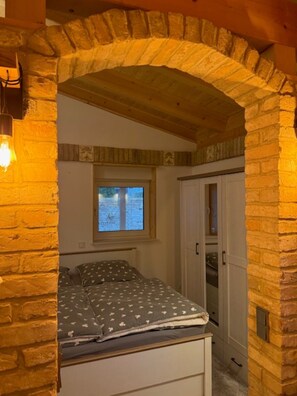 A bedroom with a stone archway, a bed with patterned bedding, a window, and a wardrobe. - Bungalow "Villa Toscana" with Private Terrace, Garden, and Wi-Fi (Teltow)