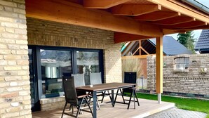 A covered patio with a wooden table and chairs, a stone pathway, and a brick wall. - Bungalow "Villa Toscana" with Private Terrace, Garden, and Wi-Fi (Teltow)