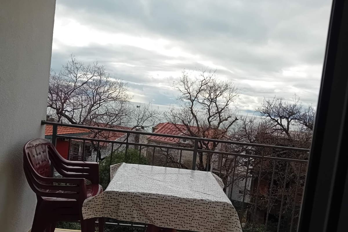 A balcony with a table and chairs, overlooking a residential area with trees and buildings.