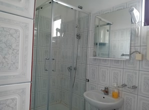 Une salle de bain avec une douche à parois de verre, un lavabo avec un miroir au-dessus et un sèche-cheveux fixé au mur.