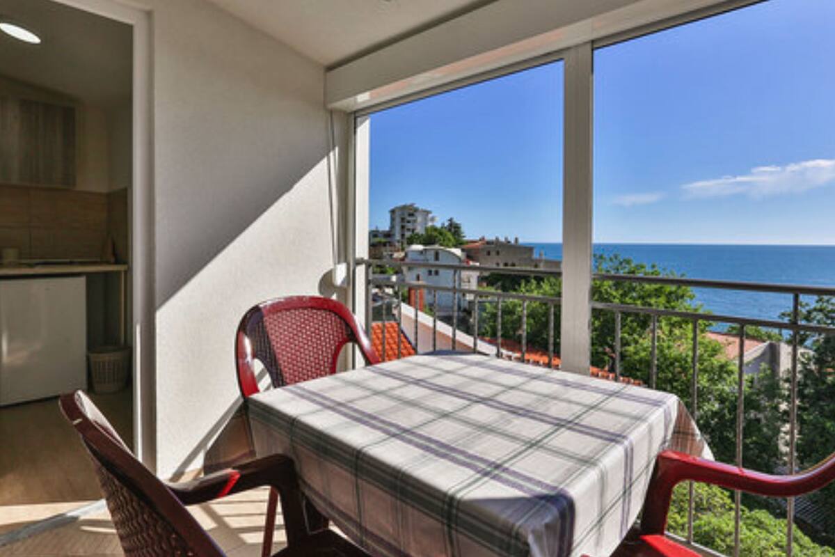 A balcony with a table and chairs, a view of the sea, and buildings in the background.