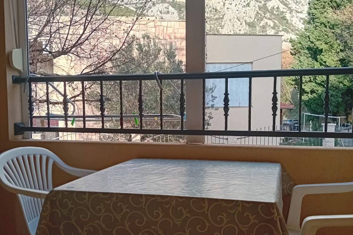 A balcony with a table and two chairs, overlooking a street with buildings and trees.