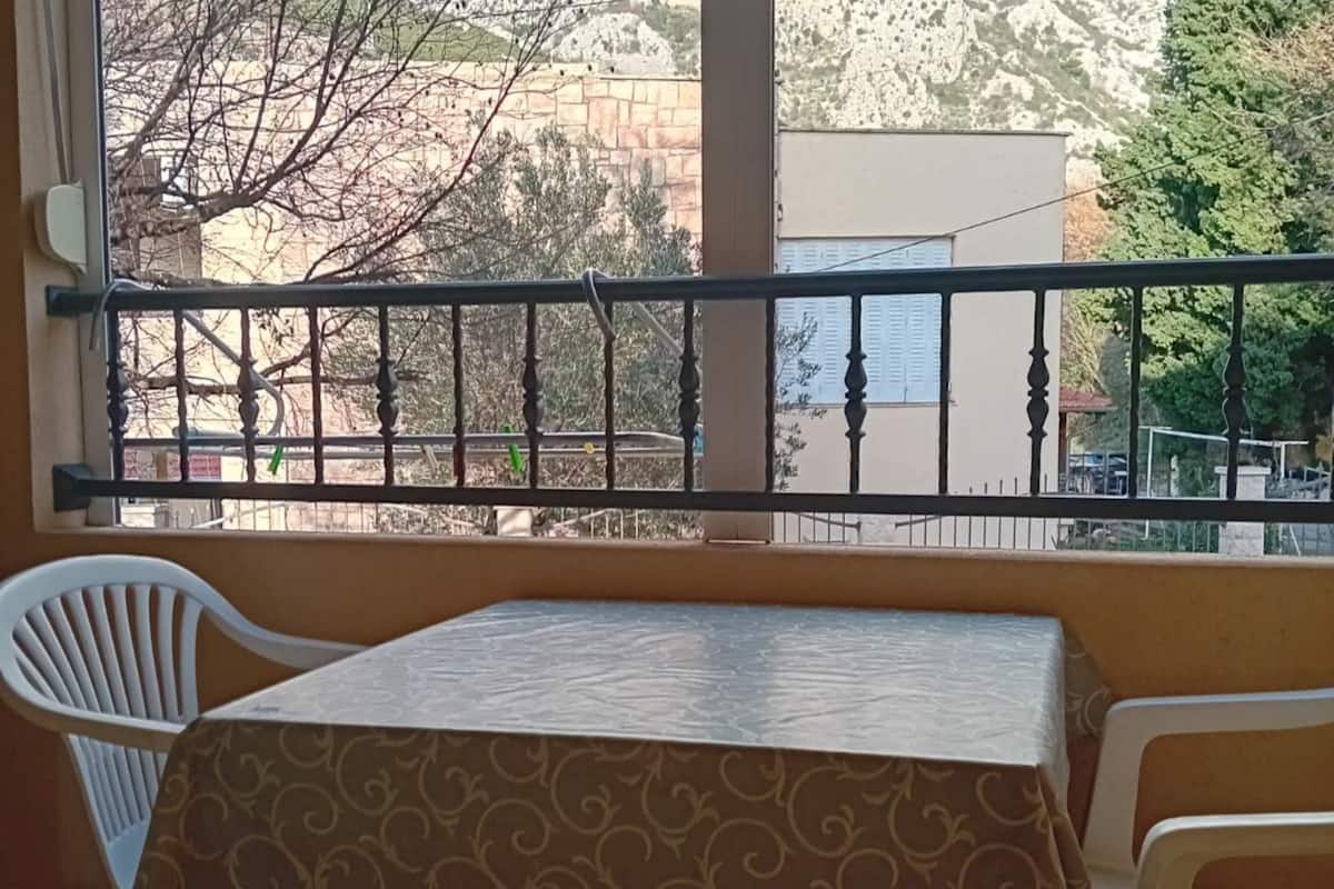 Un balcón con una mesa y dos sillas, con vista a una calle con edificios y árboles.