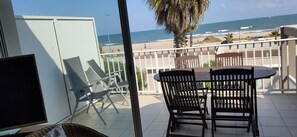A balcony with a table and chairs, overlooking a beach and the ocean. - T3 BEACHFRONT APARTMENT (Saint-Cyprien)