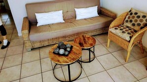 Una sala de estar con un sofá, dos mesas redondas de madera y un sillón de mimbre.
