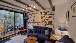 A cozy living room with a stone wall, a purple sofa, a wooden coffee table, and a view of the outdoors through large windows. - Charming House, 2 Bedrooms, Terrace & Air Conditioning (L'Escala)