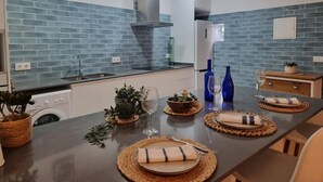 A modern kitchen with blue tiles, a stainless steel sink, and a dining area set with placemats and glassware. - Charming House, 2 Bedrooms, Terrace & Air Conditioning (L'Escala)