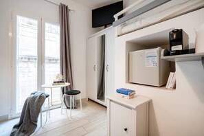 A compact room with a bed, a small table with a chair, a TV mounted above the bed, and a refrigerator with a water dispenser. - Carolina House 2 (Monopoli)