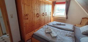 Un dormitorio con dos camas, armario de madera y una ventana con cortinas.