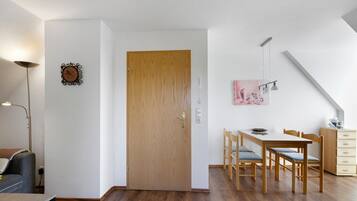 Ein Zimmer mit Holztür, einem Esstisch mit Stühlen, einer Lampe und einem Bild an der Wand.