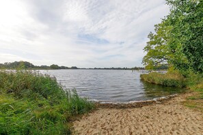 A calm lake with a sandy shore, surrounded by dense greenery and trees.