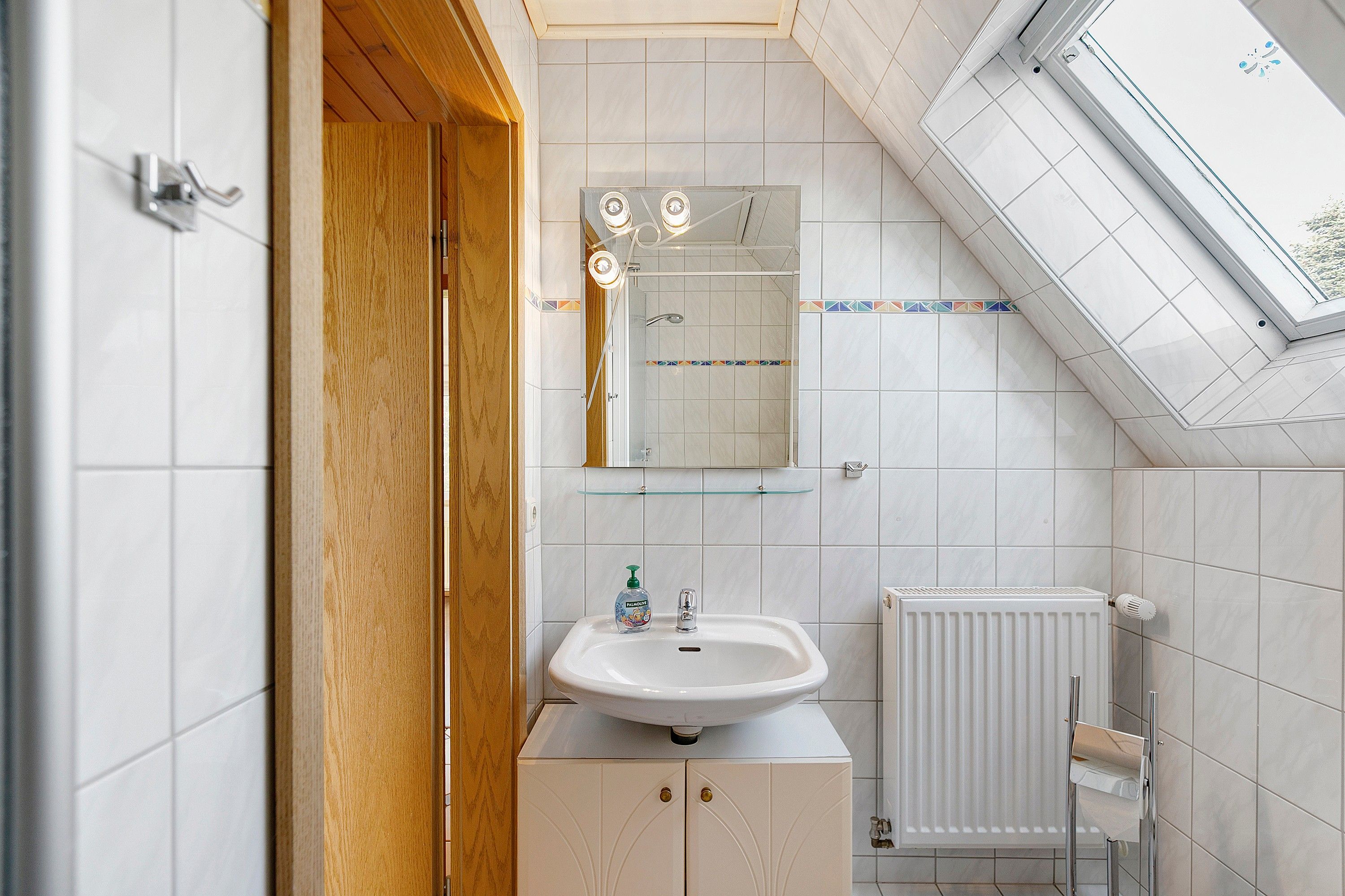 A bathroom with a skylight, a sink, a mirror, and a radiator.