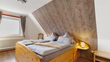 Ein Schlafzimmer mit einem hölzernen Bett, einem Nachttisch mit Lampe, einem Fenster mit Vorhängen und einer Heizung.