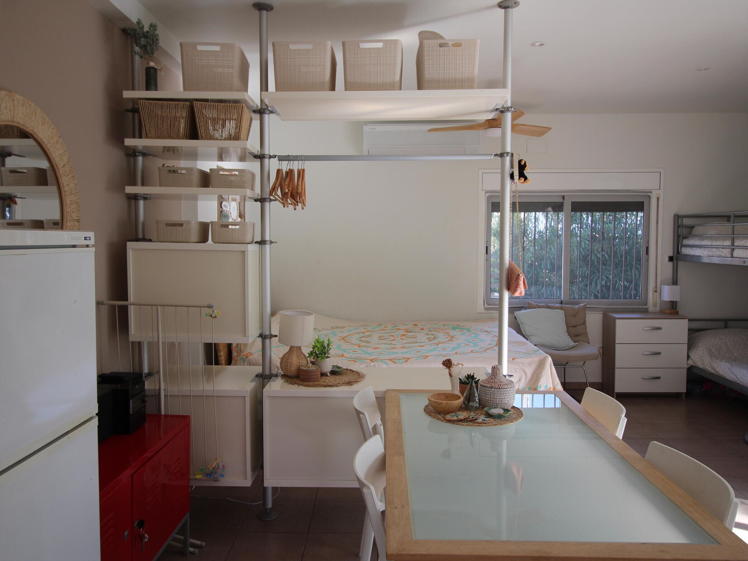 A compact, well-organized room with a bunk bed, a dining table with chairs, a small kitchen area, and a window with a view.