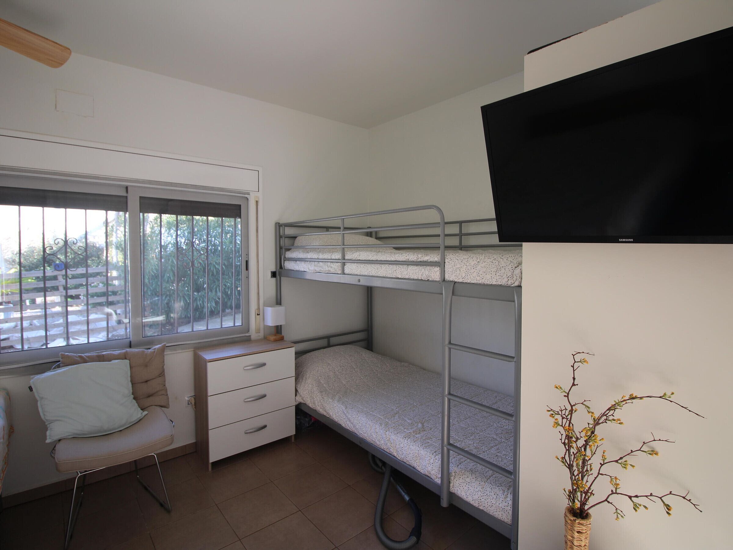 A bunk bed room with a desk, chair, window, and a wall-mounted TV.