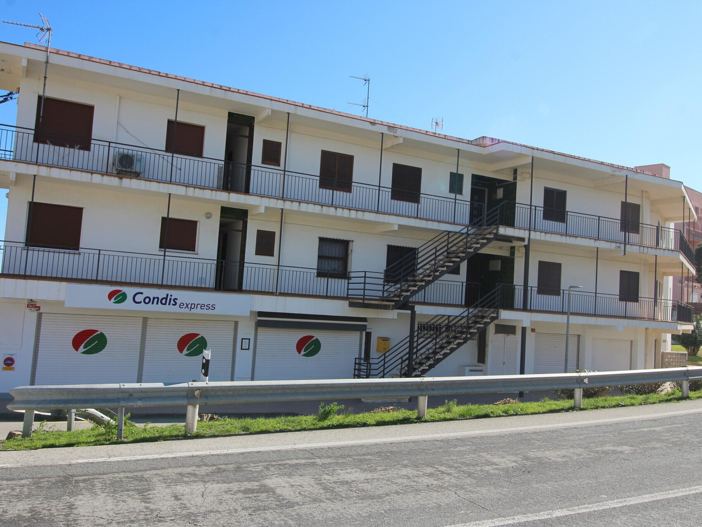 Un immeuble à plusieurs étages doté de balcons, d’une échelle de secours visible et d’une devanture de magasin avec un logo.
