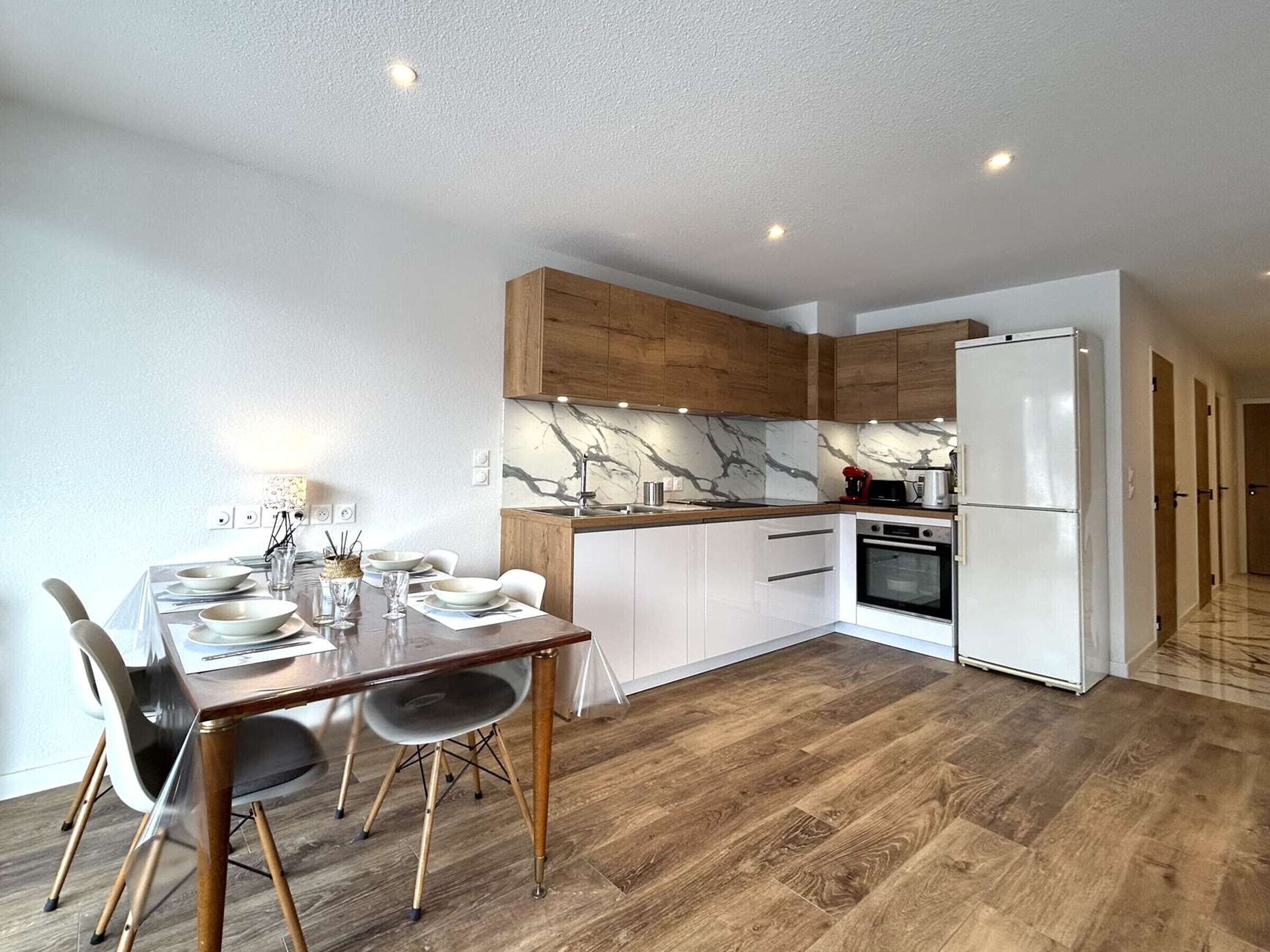 Eine moderne Küche mit weißen Schränken, einer Marmor-Spritzschutzwand und Holzdielen.