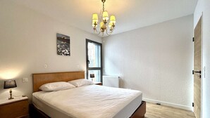 Ein Schlafzimmer mit einem hölzernen Bett, einem Nachttisch, einer Wandlampe und einem Fenster mit Blick ins Freie.