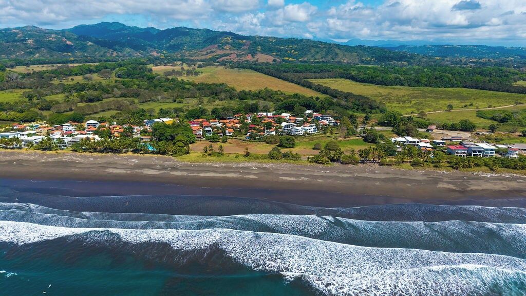 A coastal town with buildings near the beach and hills in the background.