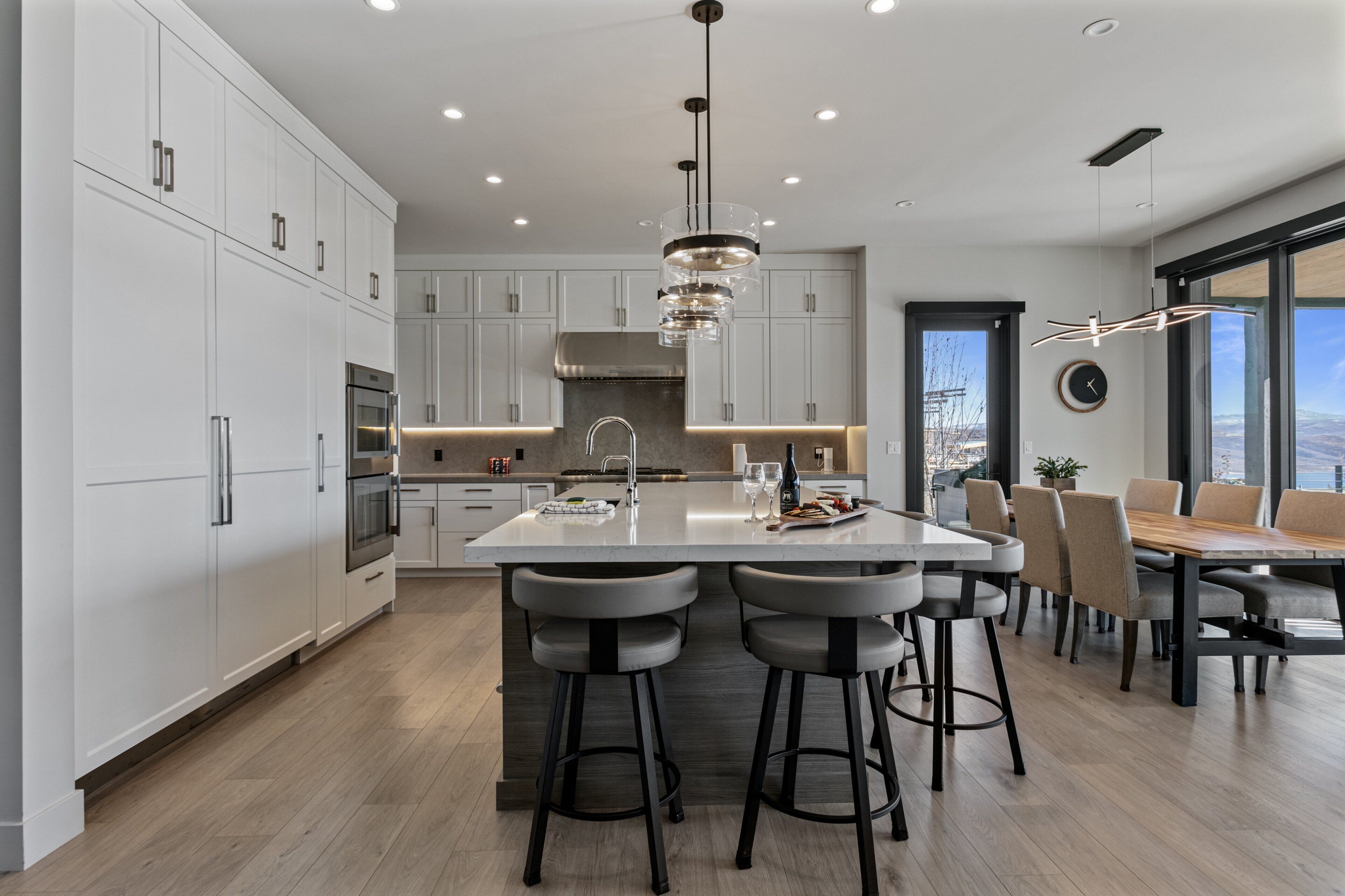 A modern kitchen with a central island, bar stools, and a dining area with a view.