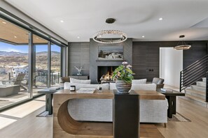 A modern living room with a fireplace, a large window overlooking a cityscape, and a staircase leading to an upper level. - Spacious Ski Getaway Hot Tub 5 Bedroom 5 Home (Heber City)