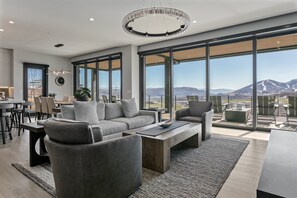 A modern living room with a large window, a sofa, a coffee table, and a dining area. - Spacious Ski Getaway Hot Tub 5 Bedroom 5 Home (Heber City)