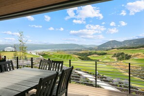 Une terrasse avec une table et des chaises donnant sur un terrain de golf et sur des montagnes lointaines.