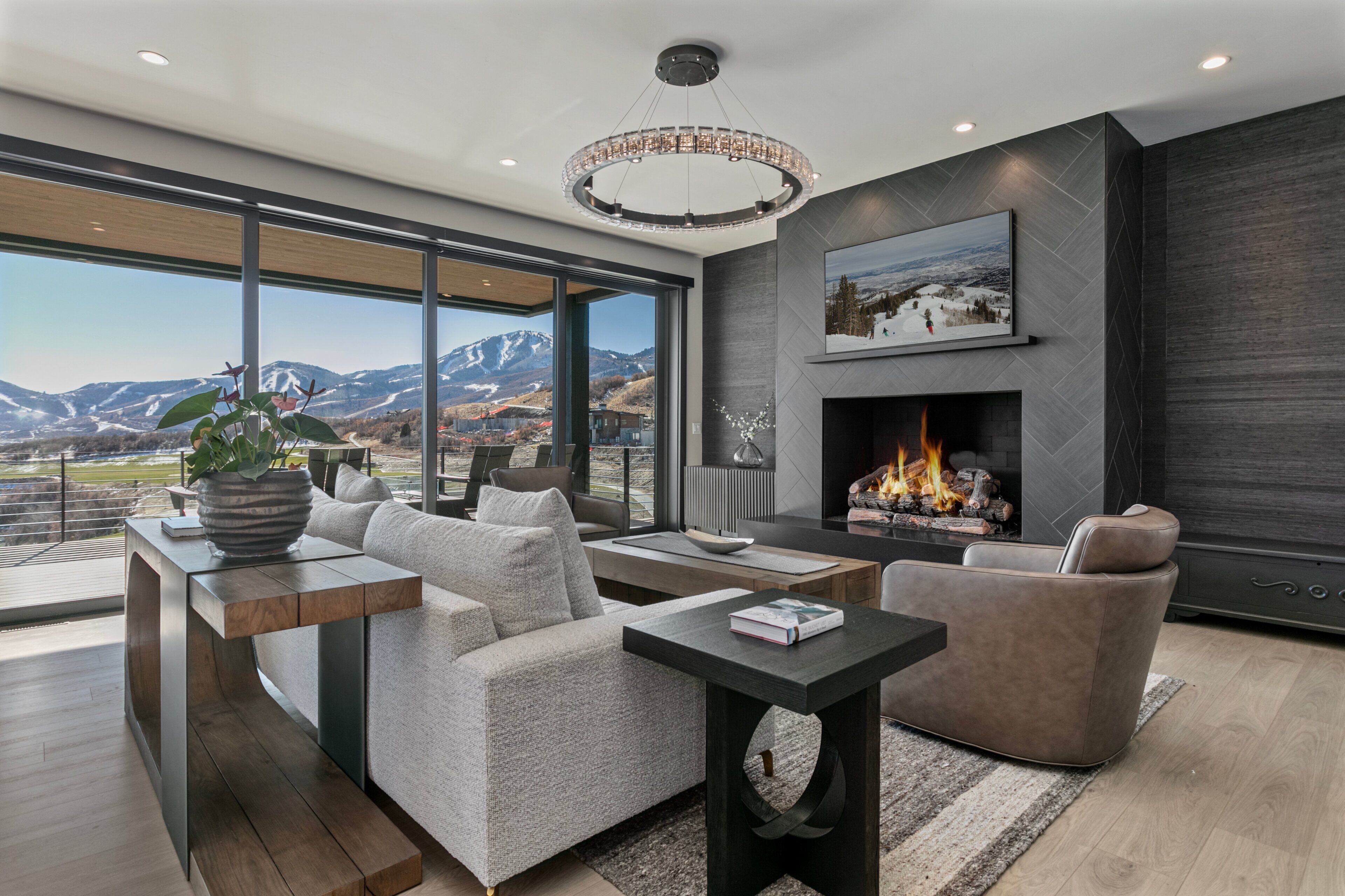 A modern living room with a fireplace, a sofa, a coffee table, and a view of mountains through large windows.