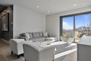 A modern living room with a grey sofa, white armchairs, and a coffee table. There is a large window providing a view of the outdoors. - Spacious Ski Getaway Hot Tub 5 Bedroom 5 Home (Heber City)