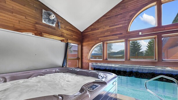 Ein Whirlpool mit Holzinnenraum, ein Schwimmbecken und große Bogenfenster mit Blick ins Freie.