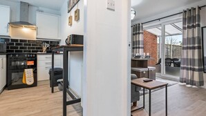 A modern kitchen with black appliances, a wooden table, and a dining area with a view of the outdoors. - Telford Centre House with Parking, Garden, Wi-Fi (Telford)