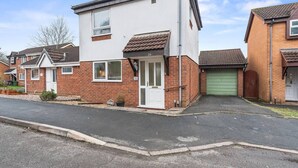 A two-story residential building with a white facade, a green garage door, and a brick exterior. - Telford Centre House with Parking, Garden, Wi-Fi (Telford)