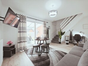 Una sala de estar moderna con un sofá, una mesa de comedor con taburetes, una escalera y un ventanal grande.