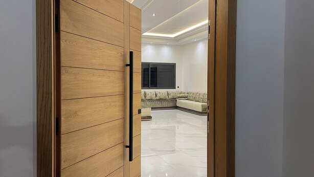 A modern interior with a wooden door leading to a living area with a sofa and a large window. - Beautiful 5-bedroom villa with AC in serene Fes neighborhood (Fes)