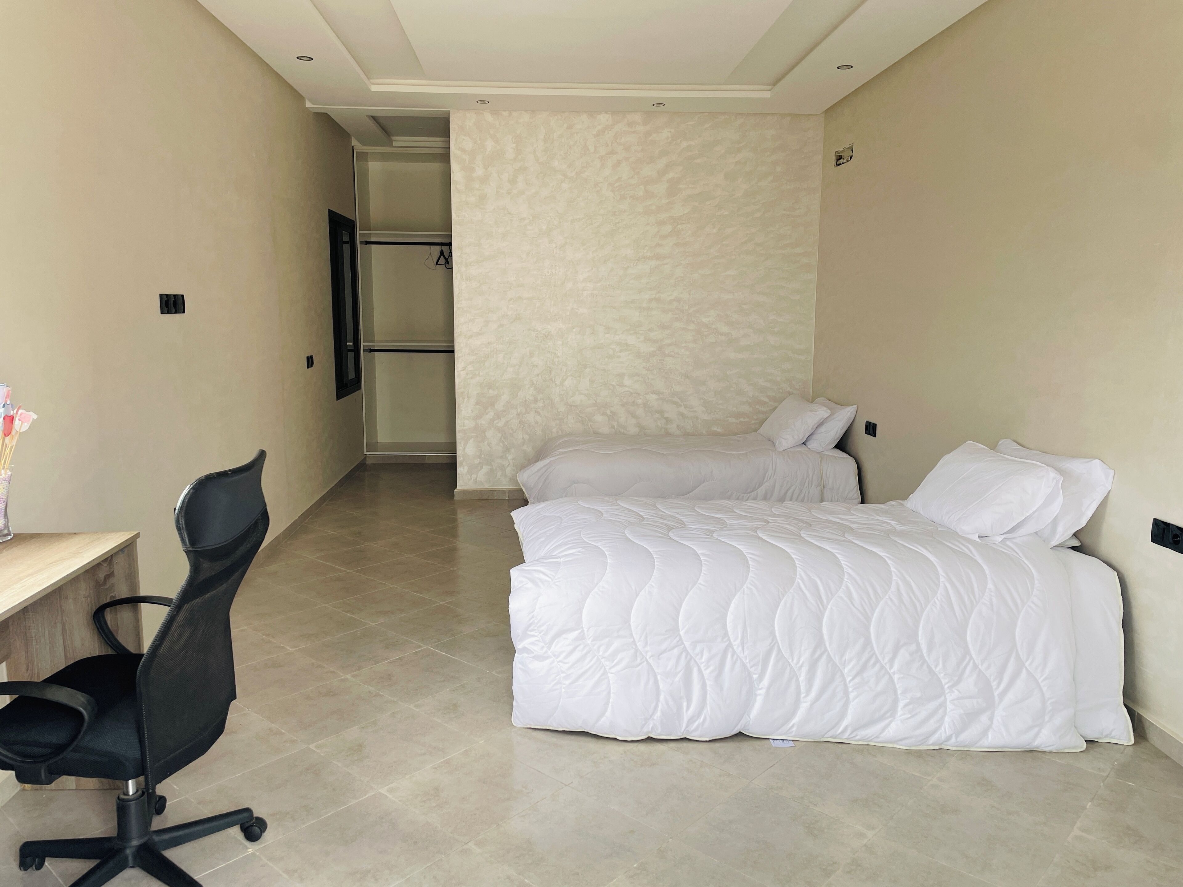 Een hotelkamer met een bureau, twee bedden, een stoel en een kledingkast.