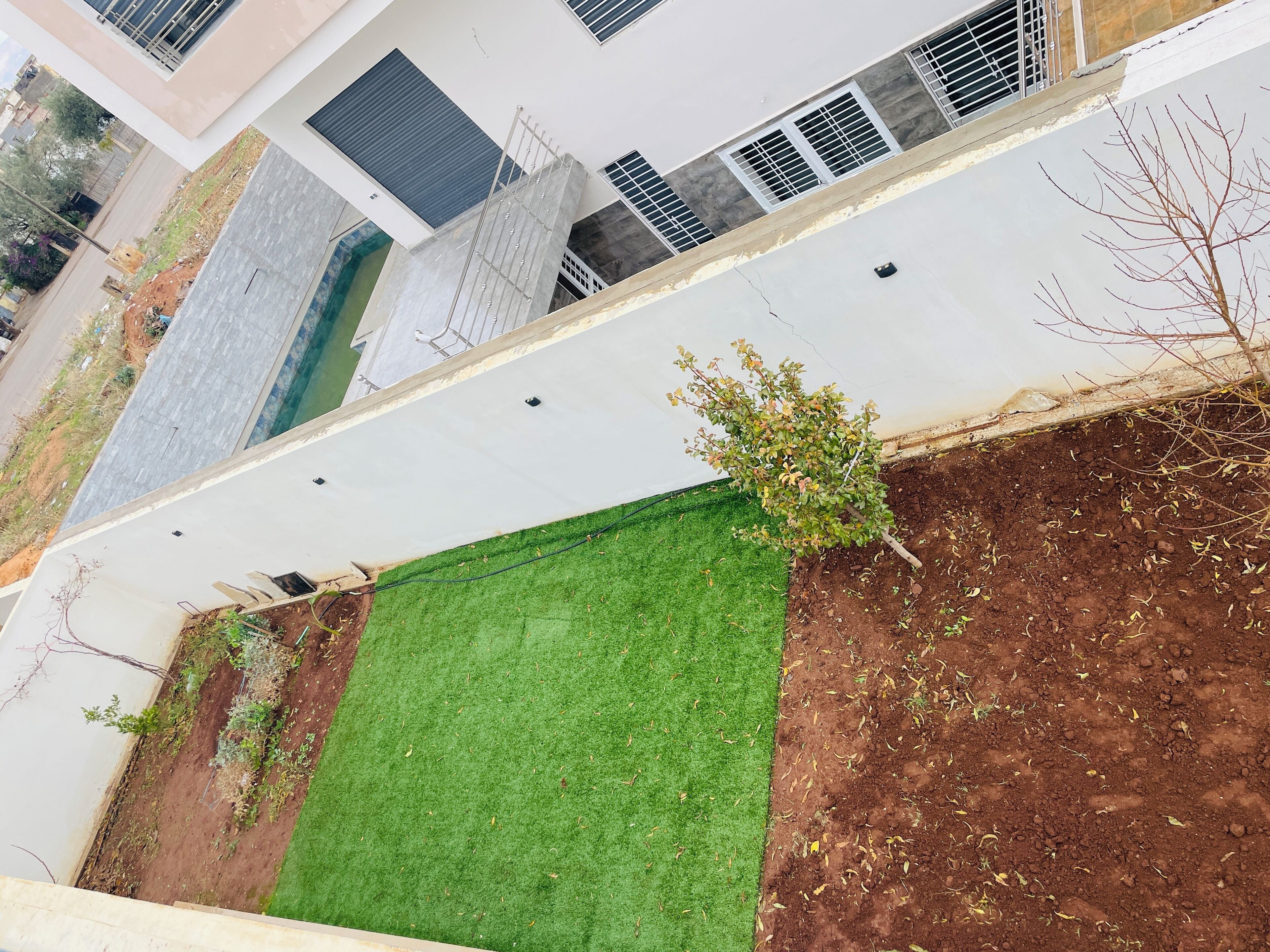 A modern building with a flat roof, a small green lawn, and a dirt area with sparse vegetation.