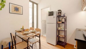 A compact kitchen with a refrigerator, microwave, and coffee maker, a dining table with chairs, and a framed picture on the wall. - This bright and stylish apartment (Bari)