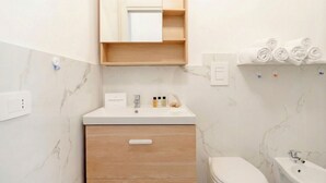 Un baño con pared de mármol, tocador de madera, inodoro y lavamanos.