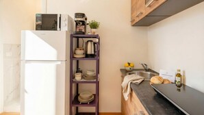 Cocina compacta con refrigerador, microondas, cafetera y una repisa con vajilla y limones.